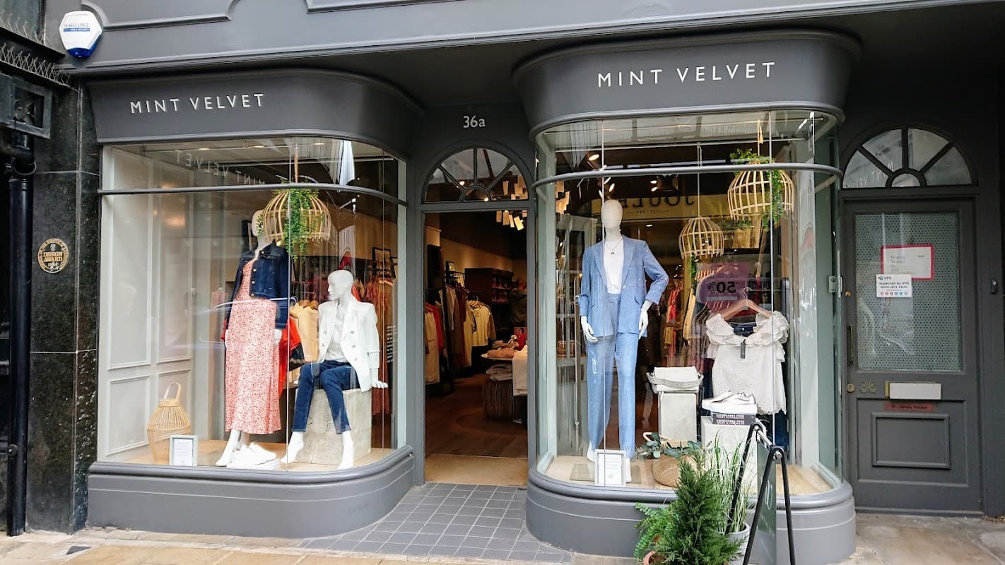 Two curved shop windows displaying clothing and accessories, with mannequins and green decor, at Mint Velvet in Harrogate.