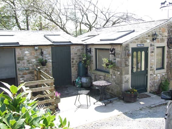 Charming stone cottage with a green door, outdoor seating, and flower pots in a rural setting.