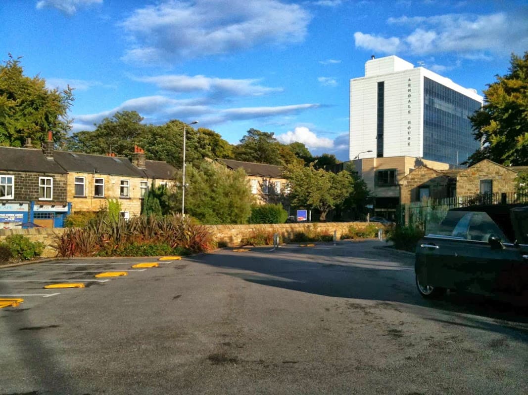 St Anne's Car Park in Headingley, featuring trees, buildings, and a modern hotel in the background under a blue sky.