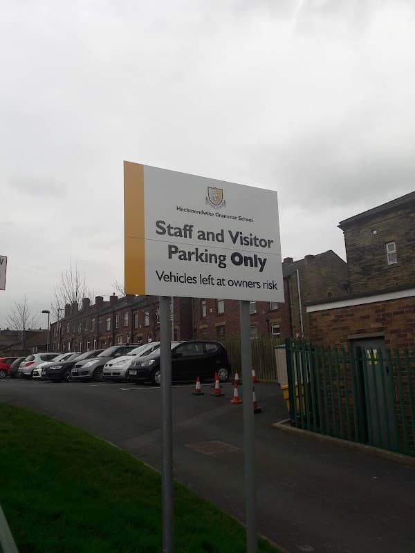 Sign for "Staff and Visitor Parking Only" at Heckmondwike Grammar School, with a view of the car park and buildings.