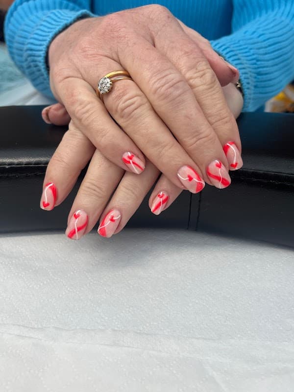 Hands with beautifully manicured nails featuring red and white heart designs, resting on a black surface.