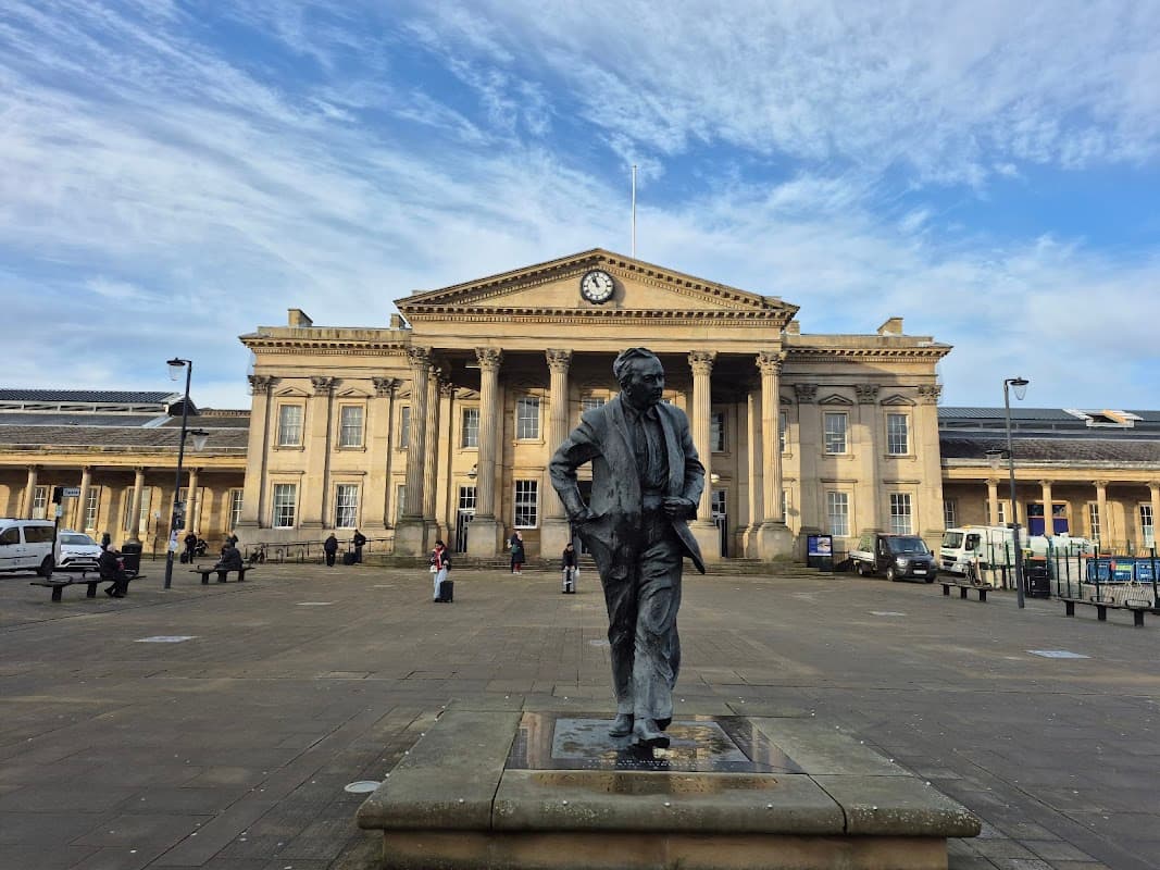 Statue in foreground with a historic building featuring columns and a clock in the background under a blue sky.