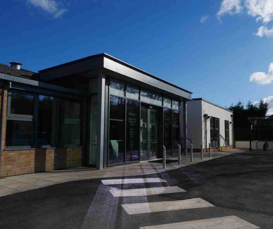 Entrance of Oaken Grove Community Centre featuring double doors, planters, benches, and a paved area.