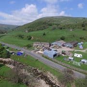 Stone building with a red roof, surrounded by green grass and dry stone walls, under a blue sky with fluffy clouds.