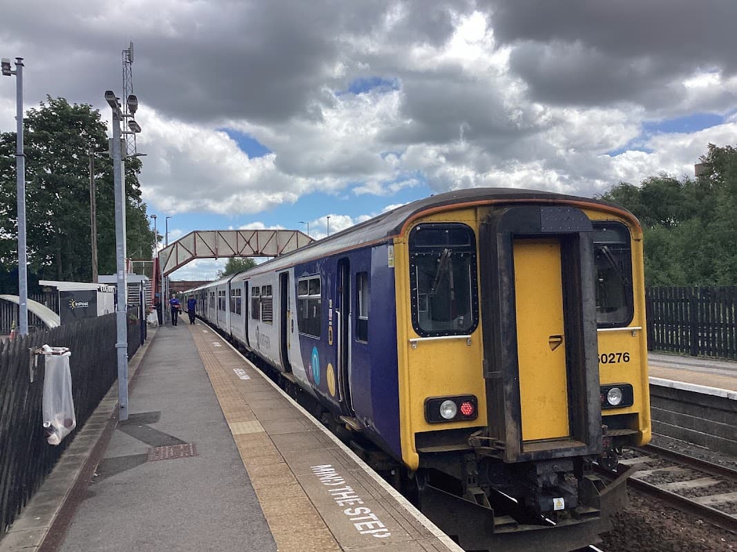 A train at Knottingley station, with clouds overhead and a bridge in the background. Passengers waiting nearby.