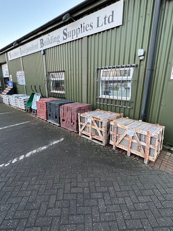 Bricks and building materials stacked outside a green metal building with "Yorkshire Independent Building Supplies Ltd" sign.