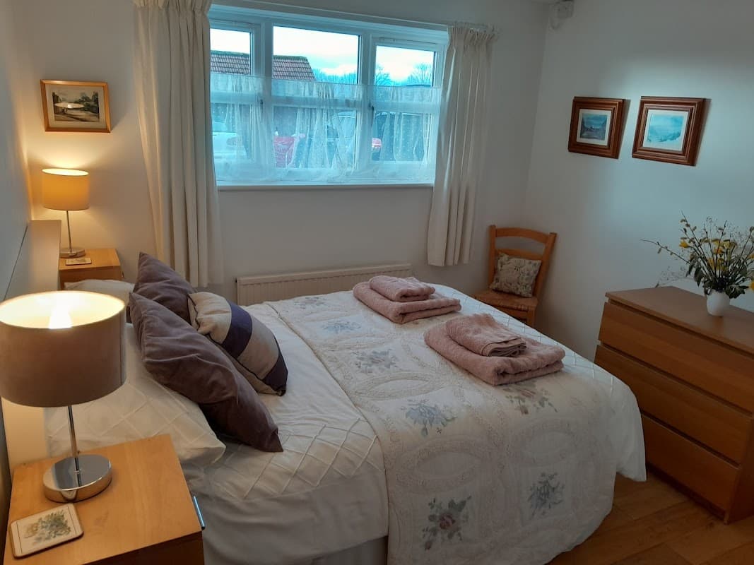 Cozy bedroom with a double bed, decorative pillows, wooden furniture, and soft lighting, featuring a window view.