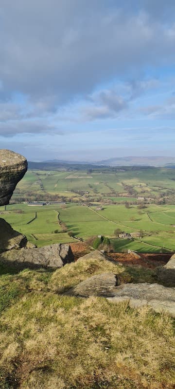Expansive green hills and fields under a blue sky with scattered clouds, framed by rocky outcrops in the foreground.