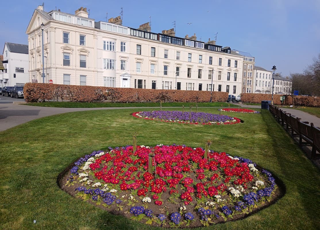 Crescent Gardens features vibrant flower beds in circular patterns, surrounded by a manicured lawn and historic buildings.