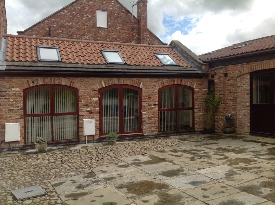 Red-brick guest house with arched windows, slate roof, and a stone-paved courtyard under a cloudy sky.