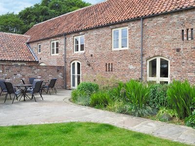 Woldsend Holiday Cottages features a brick building with a patio, outdoor seating, and lush greenery in Rillington, Yorkshire.
