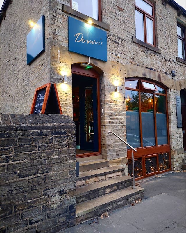 Stone building entrance with a blue sign reading "Denman's," illuminated by wall lights and featuring a staircase.