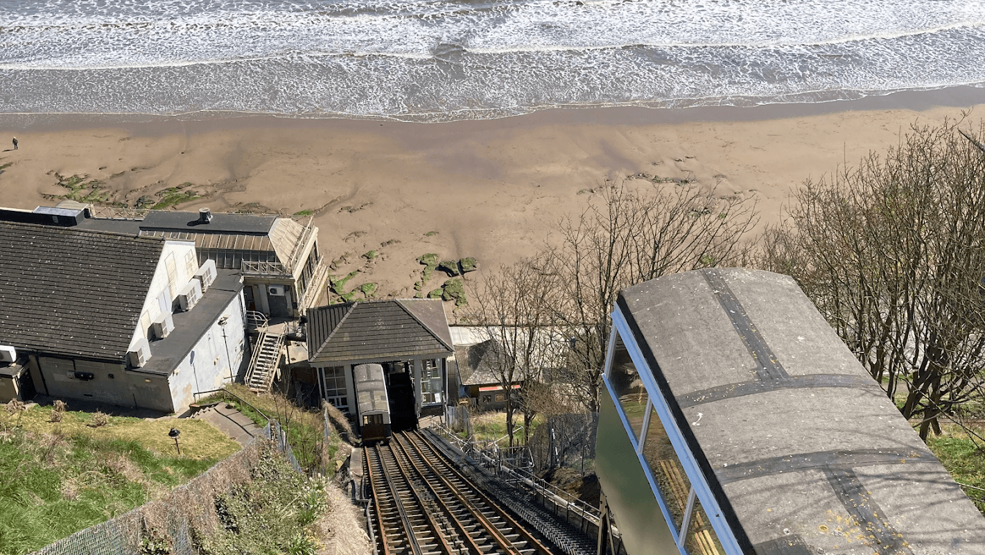 Cliff Lift tracks descend toward the beach, with the sea and sandy shore visible below, framed by greenery.