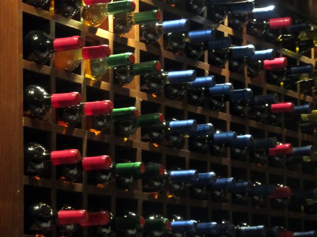 Rows of wine bottles in a wooden rack, featuring various colored caps including red, blue, and green.