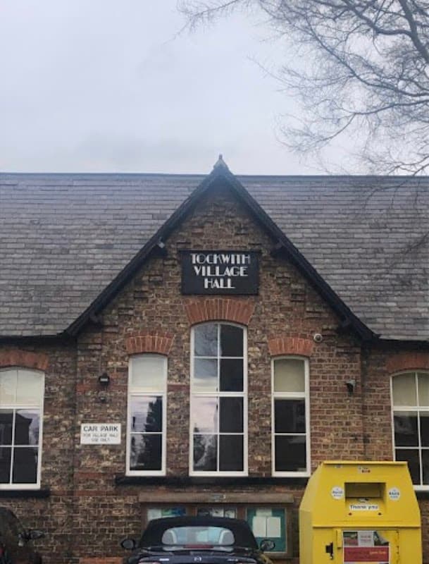 Tockwith Village Hall features a brick facade, large windows, and a yellow recycling bin in the foreground.