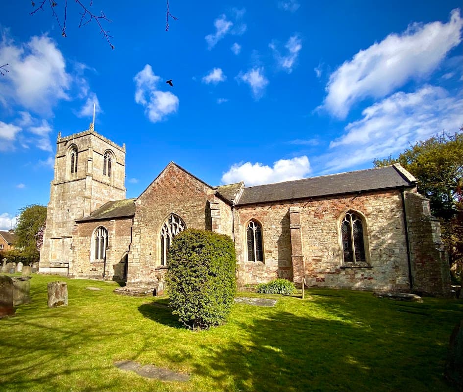 All Hallows Church features a stone exterior, a tall tower, arched windows, and a lush green graveyard.
