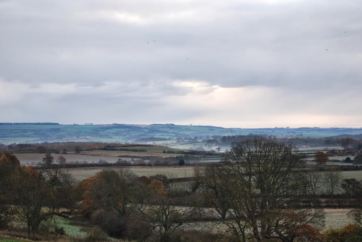 Welburn Village Hall surrounded by rolling hills and trees under a cloudy sky in the Yorkshire countryside.