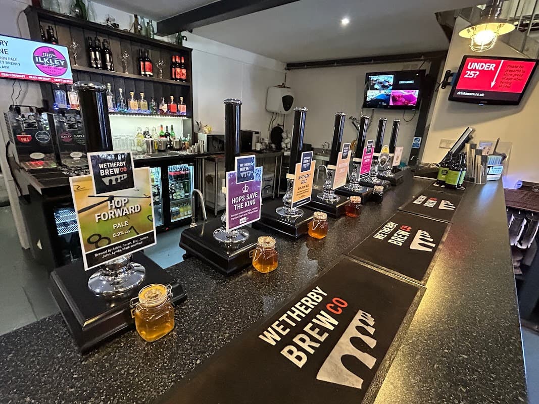Bar counter with taps, various beer labels, jars of honey, and a selection of drinks in the background.