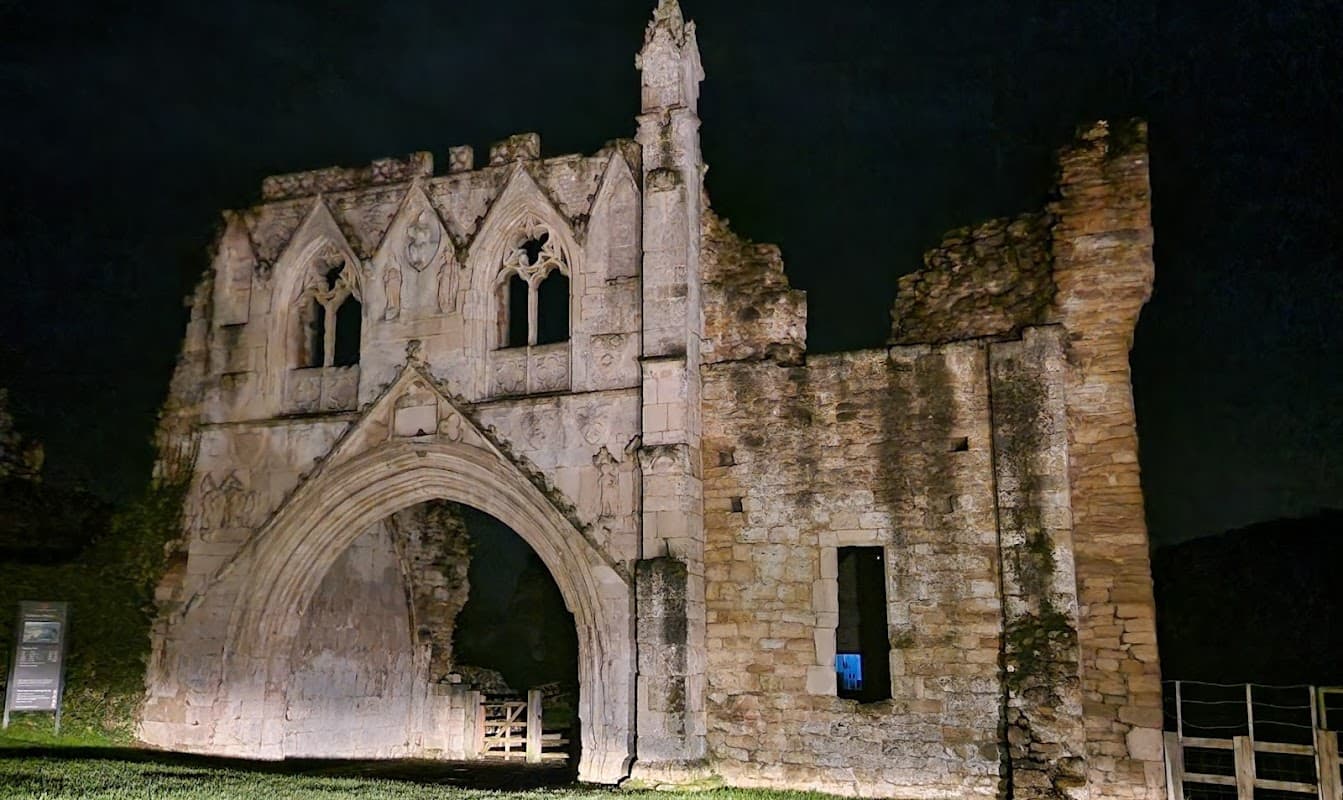 Ruins of a gothic structure at night, surrounded by grass and trees, with a sign nearby in Whitwell, Yorkshire.