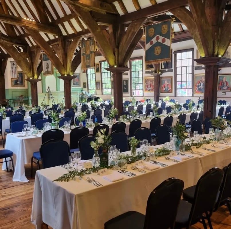 Elegant dining setup with white tablecloths, blue chairs, and floral centerpieces in a rustic hall with wooden beams.