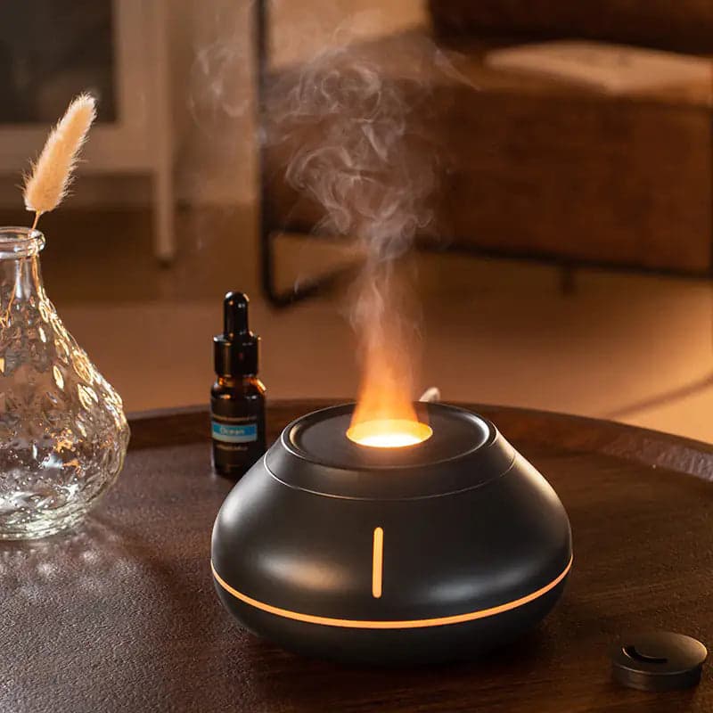 A sleek black essential oil diffuser emits steam and light, accompanied by a glass bottle and a decorative vase.