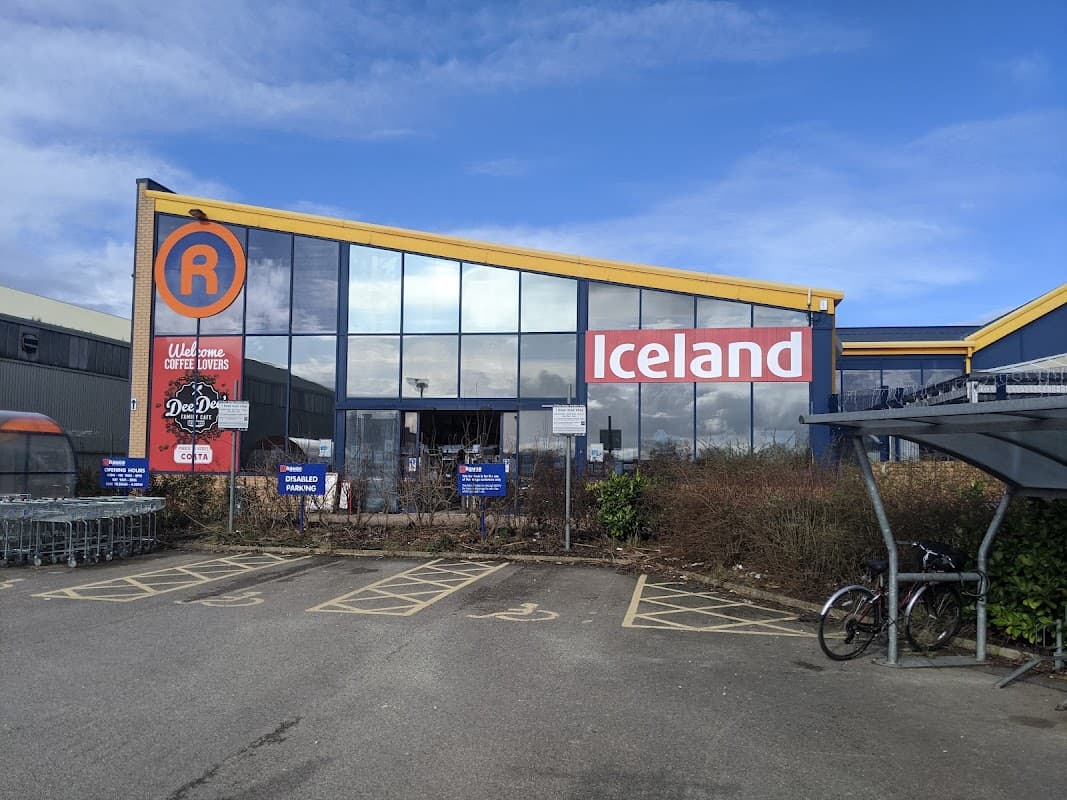 Modern storefront with large windows, featuring "Iceland" signage and a parking area with bicycle racks.