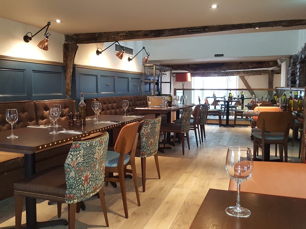 Stylish restaurant interior with wooden beams, elegant tables, and colorful patterned chairs, creating a warm atmosphere.