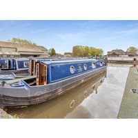 Blue narrowboat "Bella" by Hoseasons with wooden doors, circular windows, and moored on a calm canal.