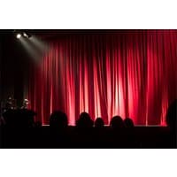 Red theater curtains illuminated by spotlight, with silhouetted audience in foreground.