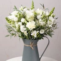 Bouquet of white roses and lisianthus in a gray ribbed metal jug with twine bow.