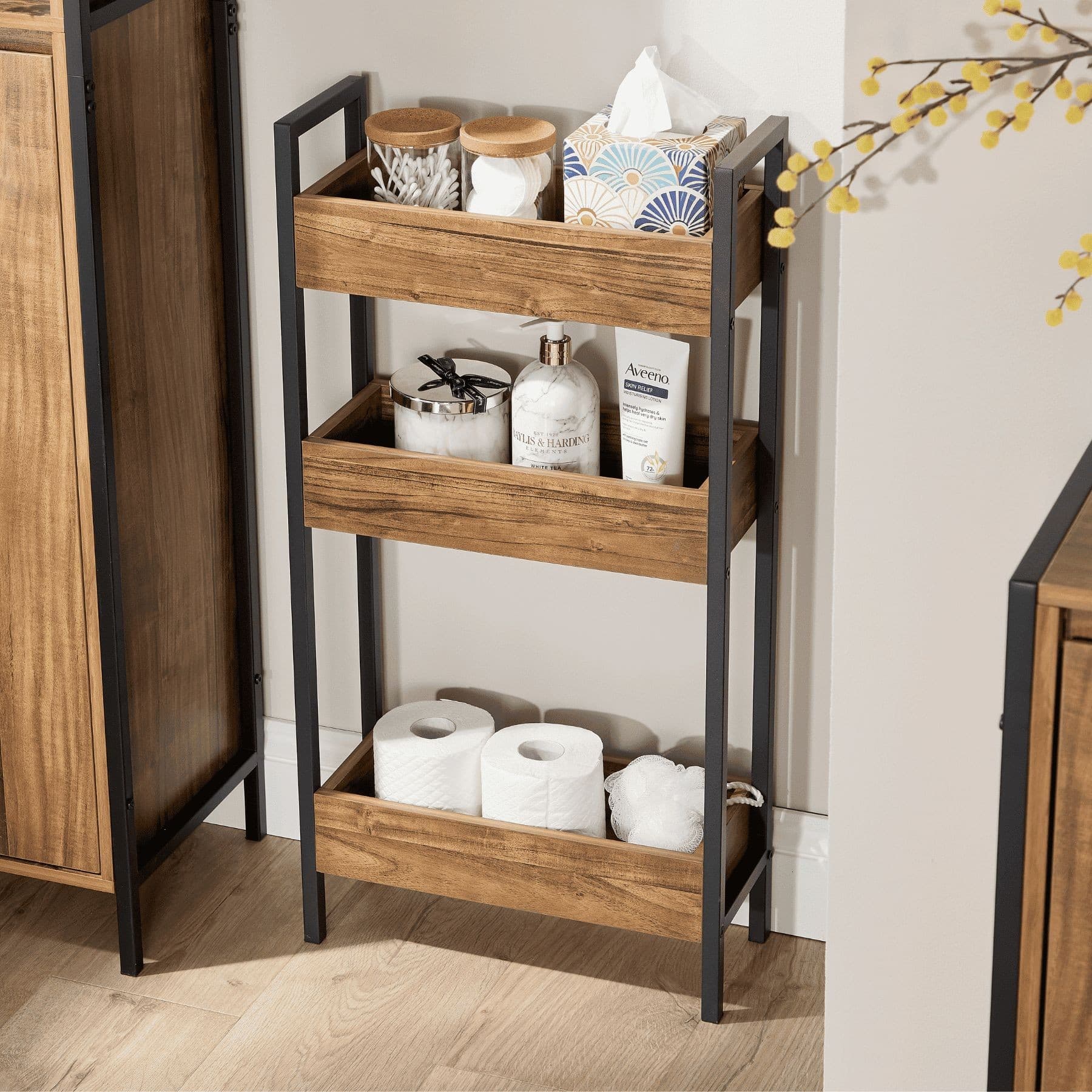 Three-tier side shelf organizer featuring a functional metal frame with a wood finish, holding decorative jars, tissue box, and bathroom essentials, set against a neutral wall.
