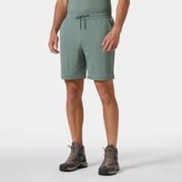 Green Helly Hansen men's shorts with drawstring waist, knee-length, lightweight fabric, worn by model with hiking boots.
