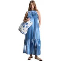 Striped blue and white maxi dress with ruffles, sleeveless design, worn by a woman holding a floral tote bag.