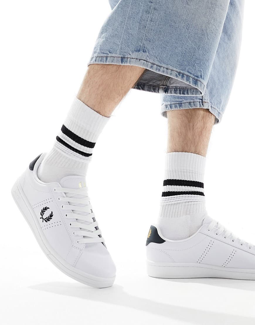 White leather trainers with a navy heel tab, featuring the iconic Fred Perry laurel logo, paired with cropped denim and striped white socks.
