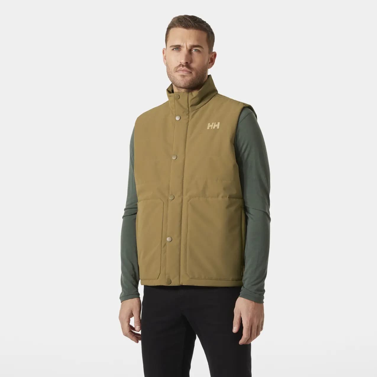 Sleeveless khaki jacket by Helly Hansen, featuring a high collar, front snap buttons, and a subtle logo on the chest, paired with a long-sleeve green shirt underneath.