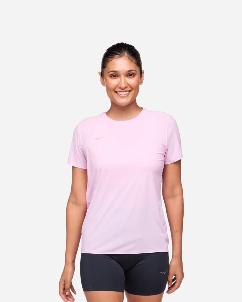 Light pink short sleeve running shirt for women, made from breathable material, featuring a round neckline and HOKA logo, paired with black shorts. Size XS.