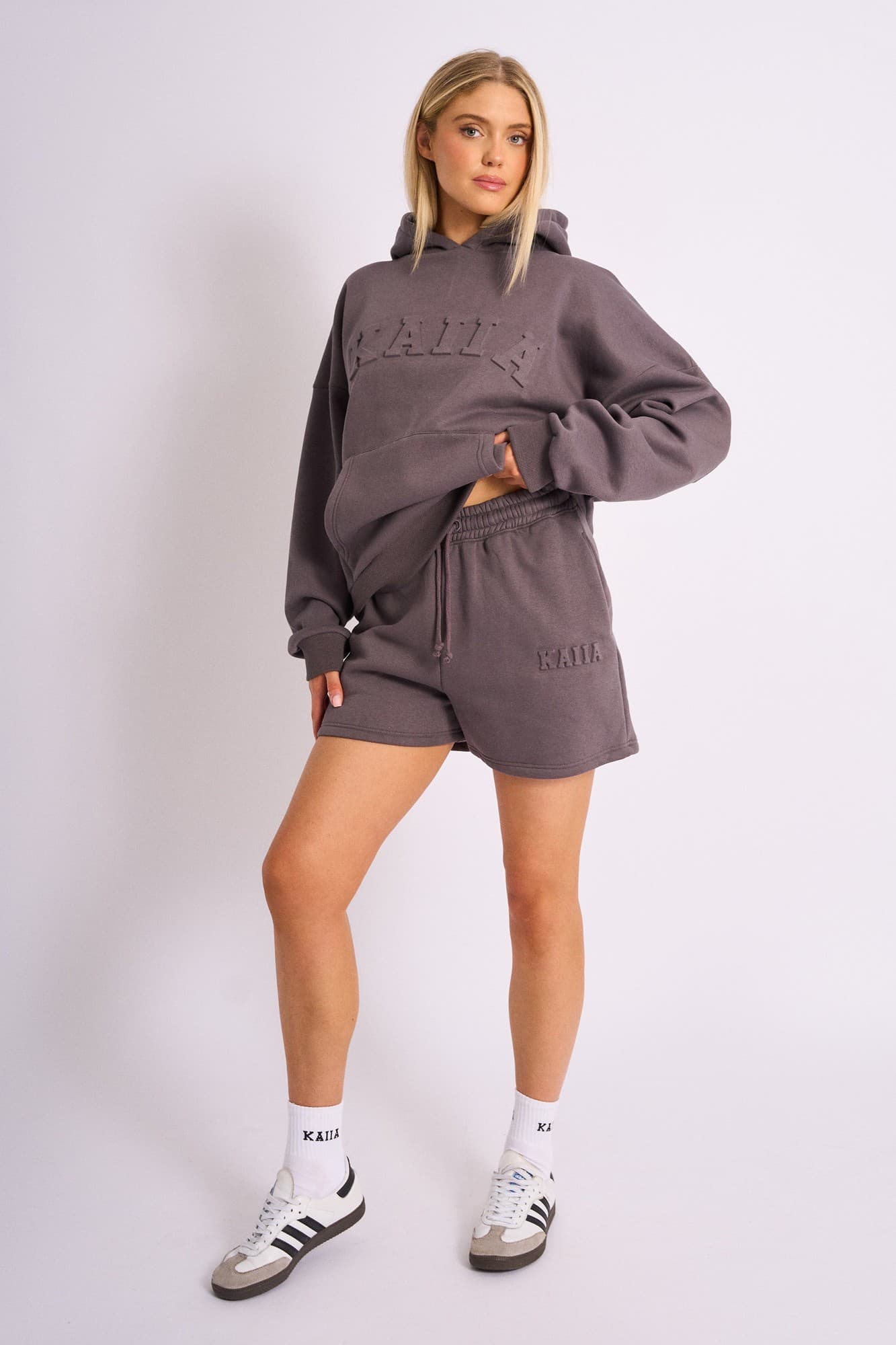 Dark grey sweat shorts featuring an embossed "Kaiia" logo on the front, made from soft material, styled with a drawstring waist and paired with a matching hoodie.