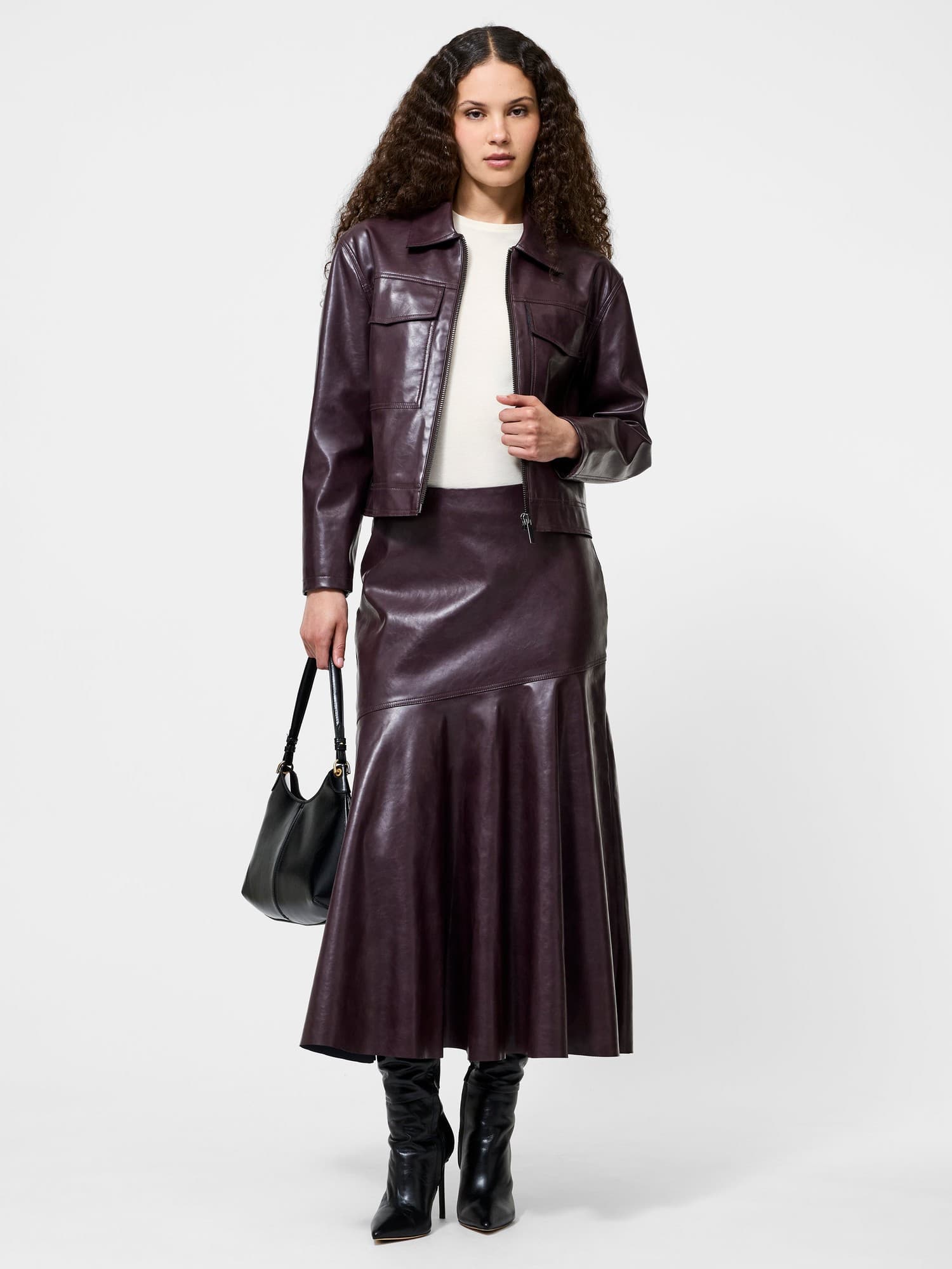 Burgundy faux leather midi skirt with a flared hem, paired with a matching jacket, styled with a cream top and black accessories, featuring a sleek silhouette.