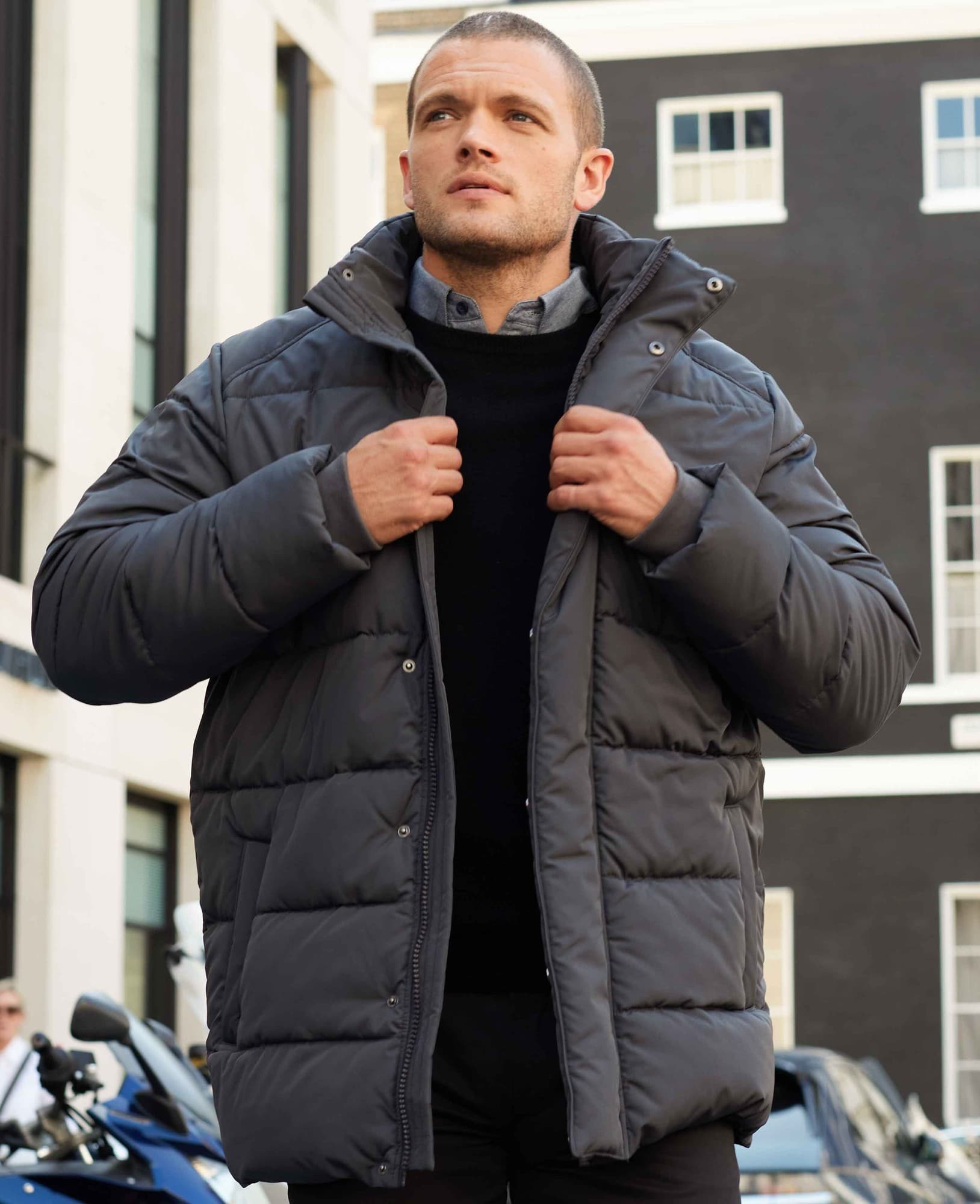 Men's dark grey hooded puffer jacket featuring rib knit storm cuffs, zip closure, and a relaxed fit, worn by a model outdoors. Size: Large.