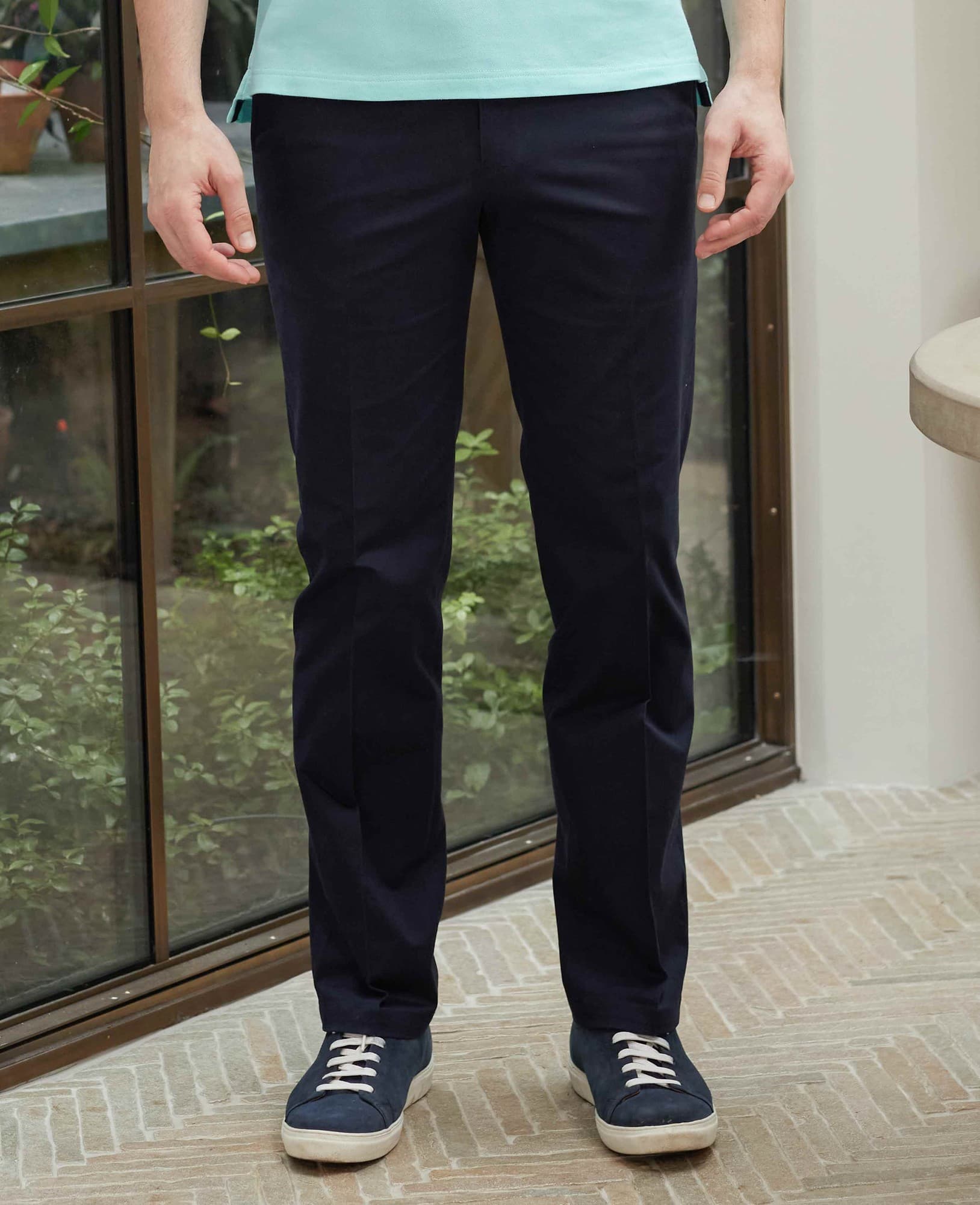 Men's navy stretch cotton chinos with a classic fit, flat front design, and size 34" x 30", styled with a light blue shirt and casual sneakers.