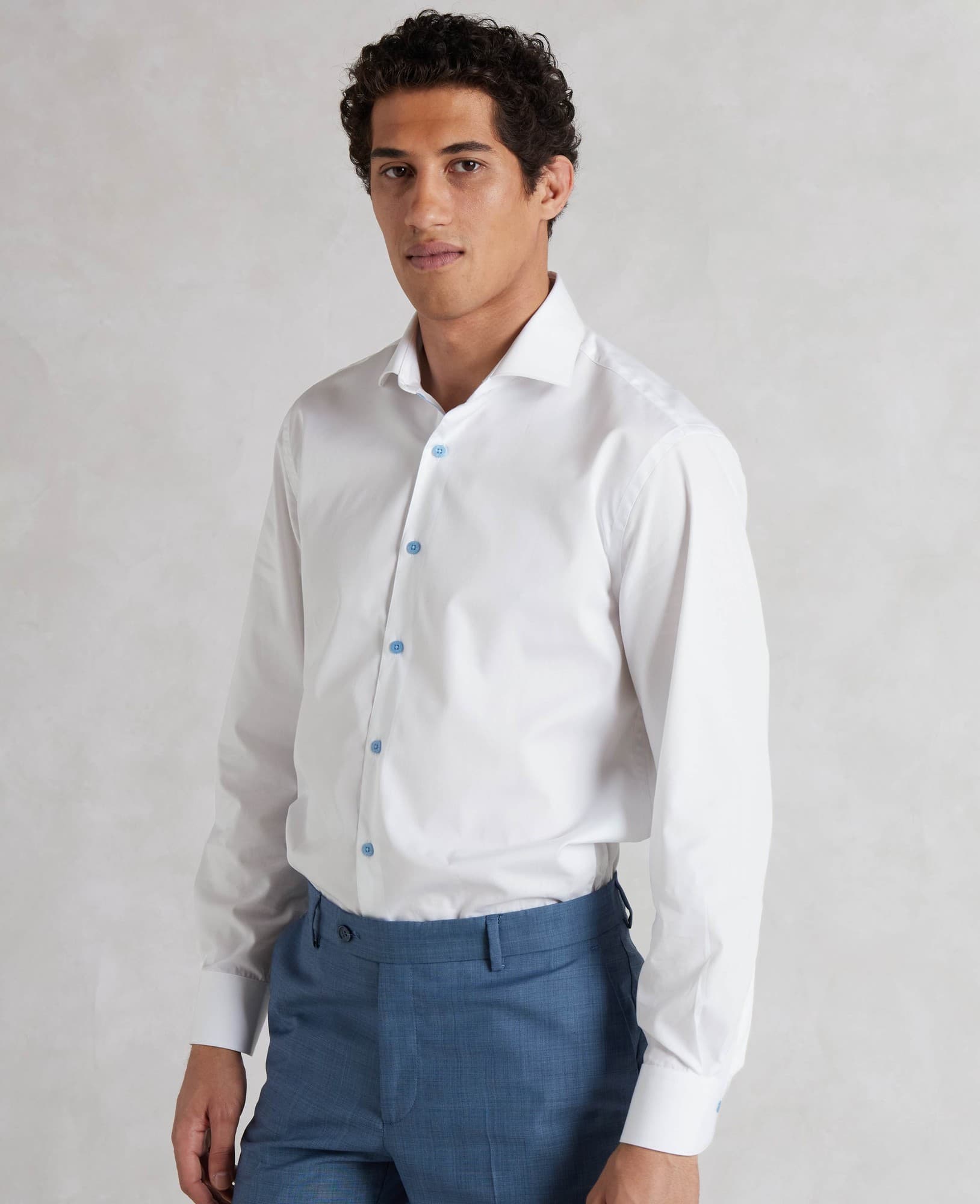 Men's white slim fit shirt featuring blue buttons, single cuff design, made from smooth fabric, displayed on a model wearing blue trousers, size large extra long.