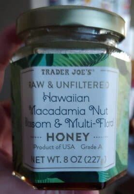Glass jar with a gold lid, labeled "Hawaiian Macadamia Nut Blossom & Multi-Floral Honey," featuring green tropical leaf designs and a white background, 8 oz size.