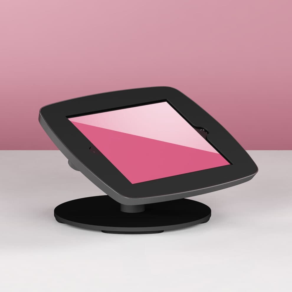 Black Bouncepad Counter stand for Apple iPad 5th Gen 9.7 (2017) with an angled display, featuring a sleek design and a sturdy circular base on a light surface against a pink background.