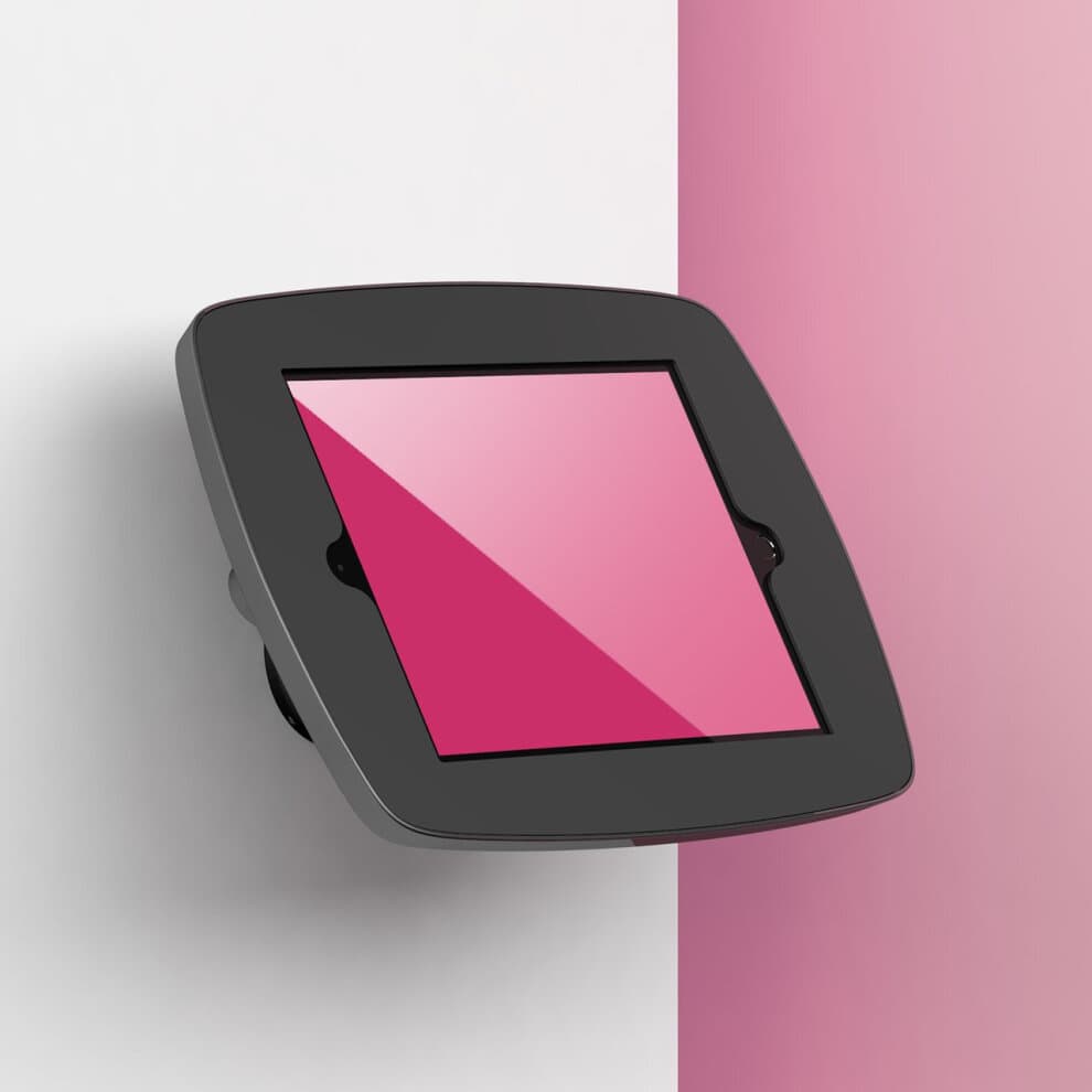Black Bouncepad Wallmount for Apple iPad 5th Gen 9.7 (2017) securely holds the device, featuring a sleek design with a glossy screen and a modern finish against a pink background.