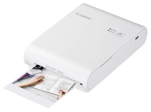 Canon SELPHY SQUARE QX10 portable wireless photo printer in white, featuring a textured surface and a print emerging from the front, showcasing vibrant color output.