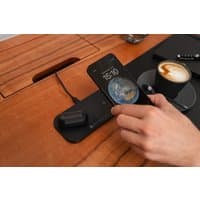 Black dual wireless charging pad with two devices charging, sleek design, wooden desk background.