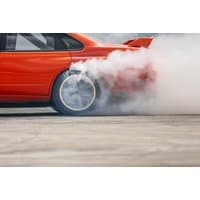 Red rally car drifting with smoke billowing from rear tires on a track.