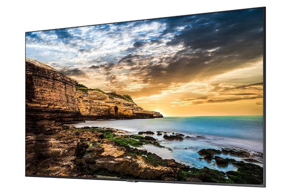 Samsung 65" Crystal UHD 4K Signage QE65T features a sleek black frame, ultra-thin design, and vibrant display showcasing a scenic coastal landscape at sunset.