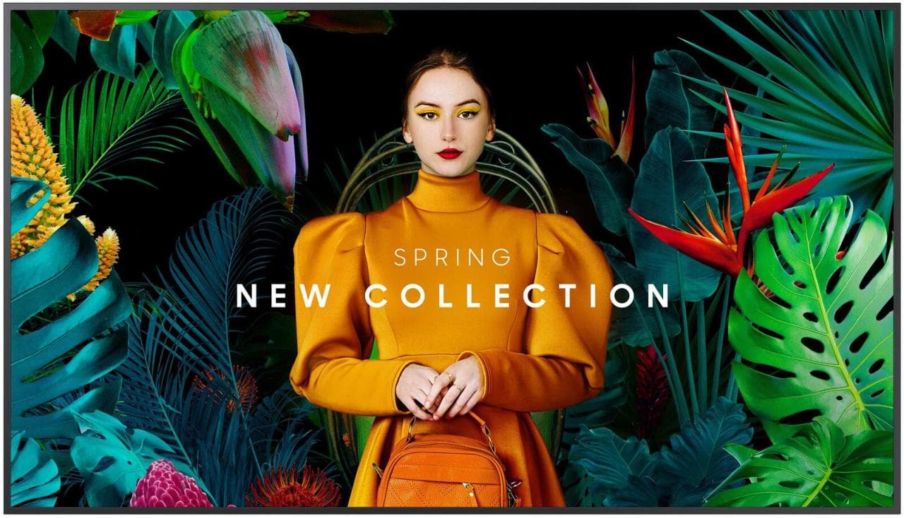 Samsung QB85C 85" LCD flat panel with vibrant colors, featuring a model in a mustard yellow dress against a tropical backdrop, showcasing "Spring New Collection" text prominently.
