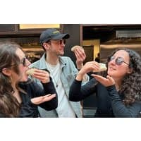 Three people enjoying tacos, wearing sunglasses, in a lively street setting, promoting a London food walking tour.